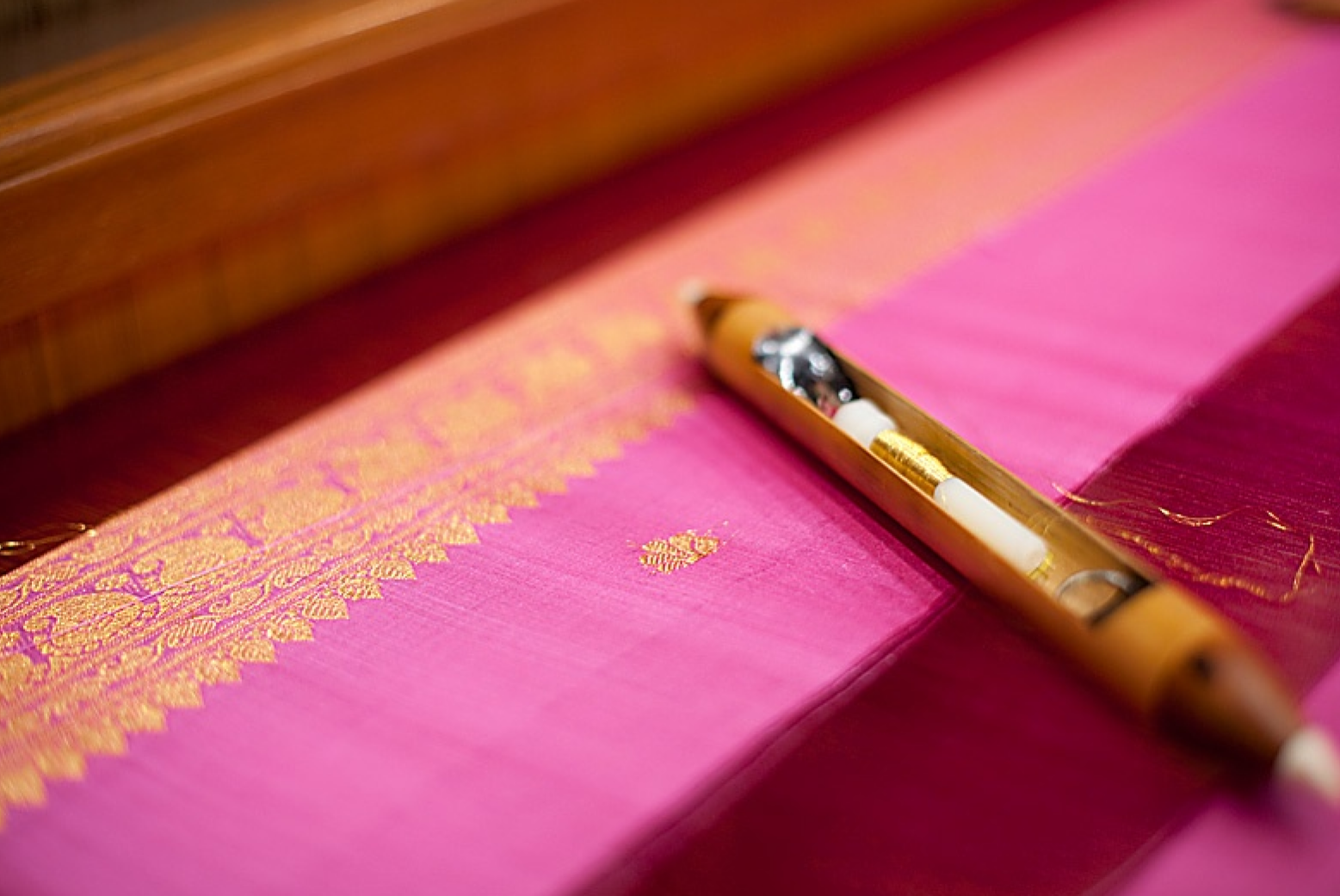 Close-up of pink saree with gold woven border beside a handloom shuttle