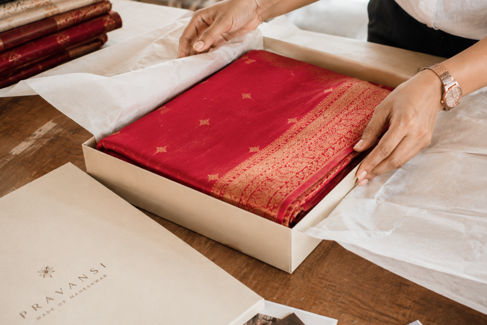 Red saree with gold motifs and ornate woven border being packed in a Pravansi box
