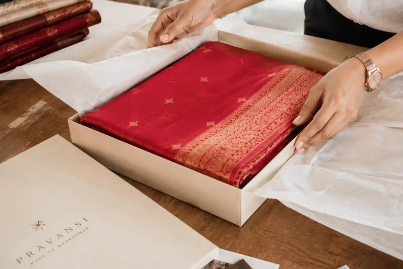 Red saree with gold motifs and ornate woven border being packed in a Pravansi box
