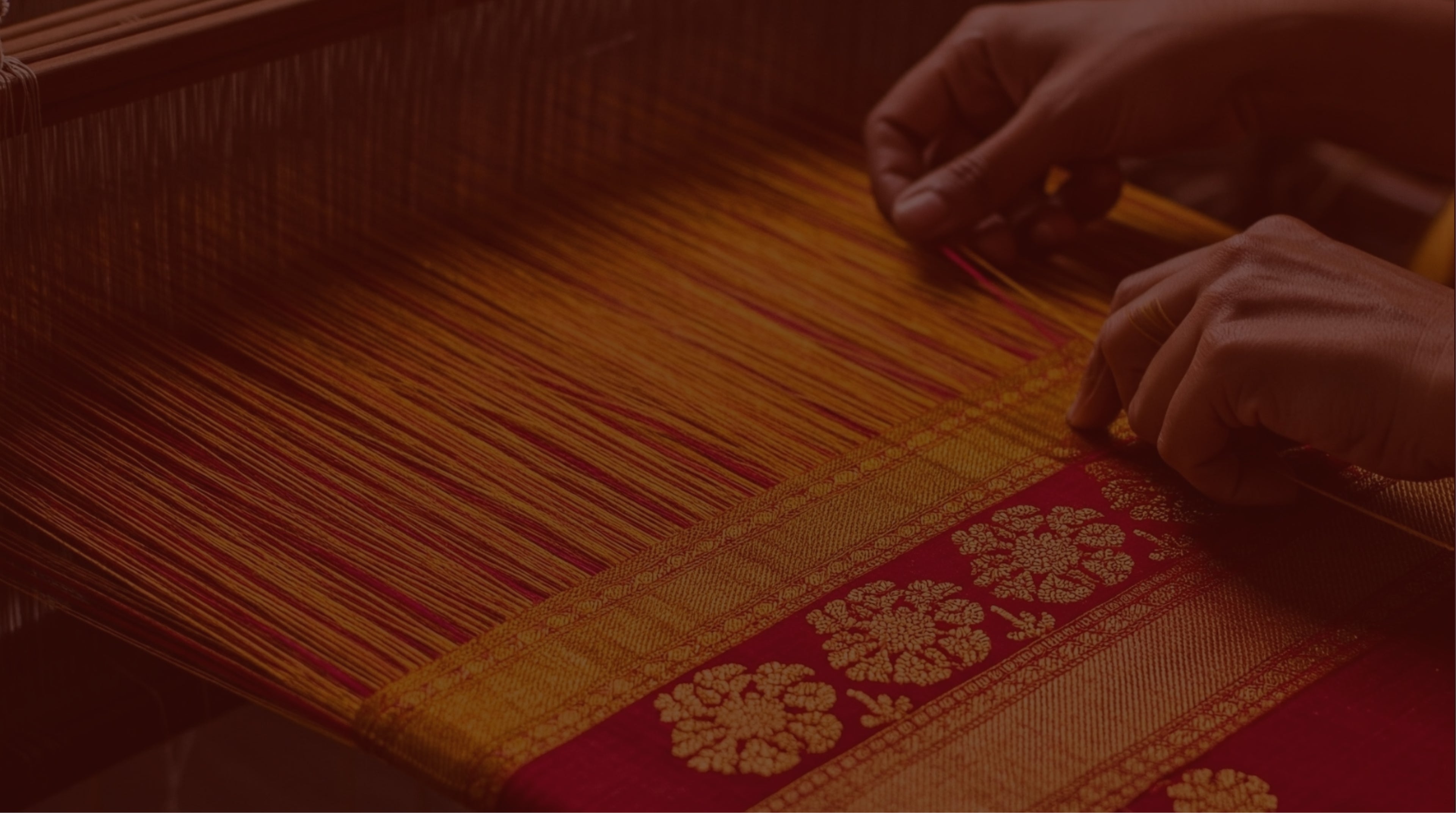 Hands weaving red and gold textile on a traditional handloom
